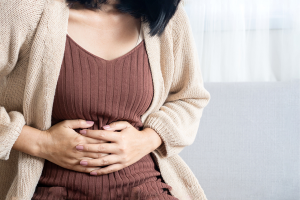 Imagen de una persona que se sostiene el estómago y experimenta problemas de salud intestinal propios de las mujeres